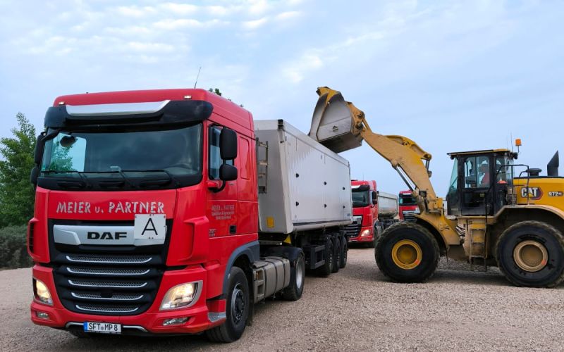 The yellow dump truck unloading material on a construction site under a clear sky.